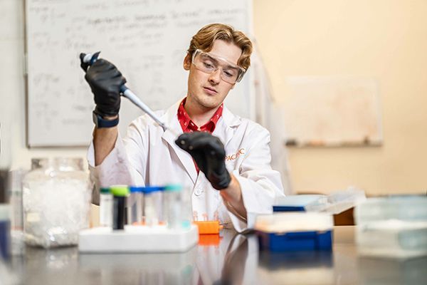 Student holding a pipette in a research lab.