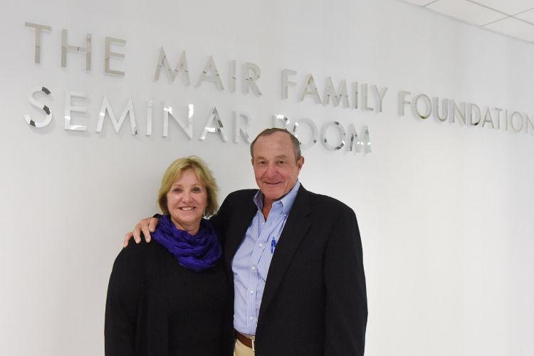 Gretchen and Jim Mair standing in front of wall reading "The Mair Family Foundation Seminar Room"