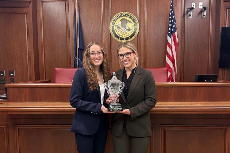 two students stand in a courtroom holding a trophy