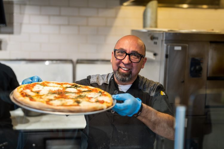 chef holds pizza up while standing in kitchen