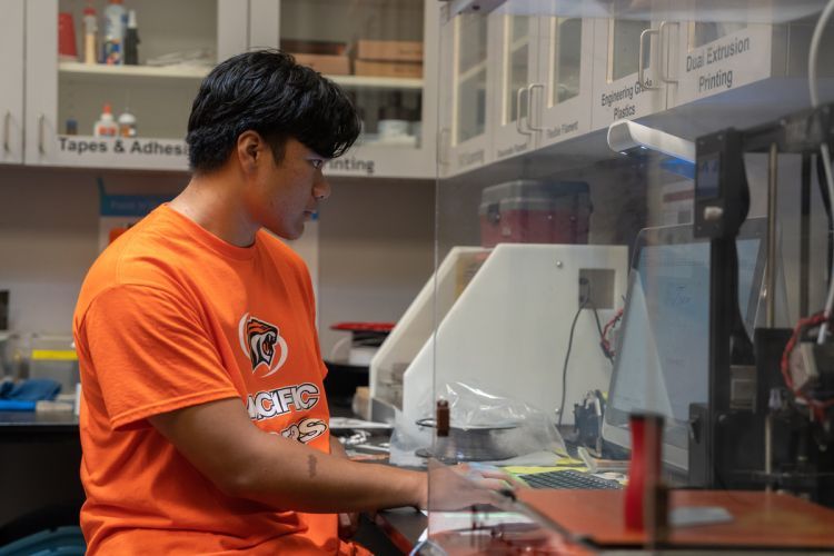 student stands at 3D printer