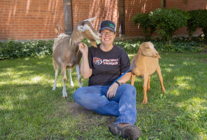 Melanie Felmlee sitting in grass with two goats.