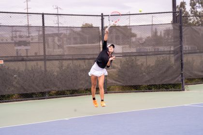 A student serves a ball on a tennis court