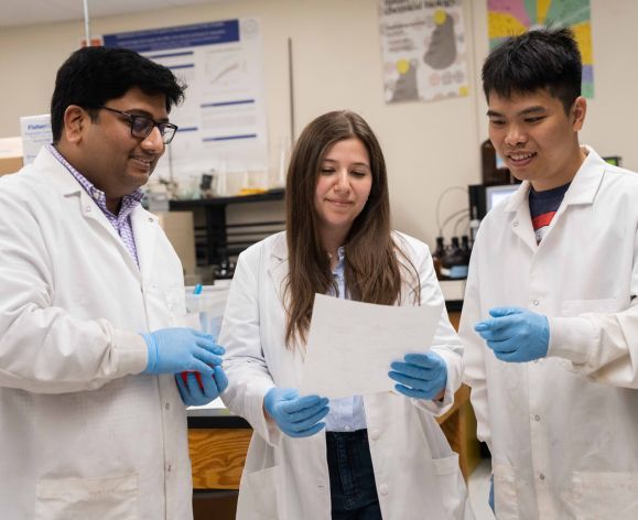 Three pharmacy students in a lab looking at a paper.
