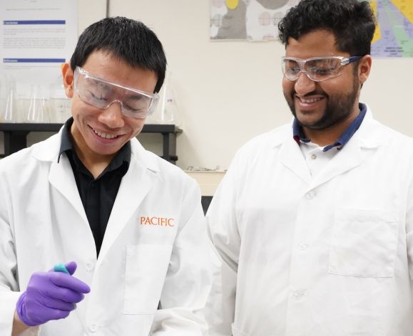 Two PCSP graduate students in a research lab wearing white coats 
